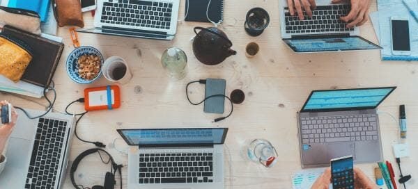 A couple of laptops on the table with people working on them